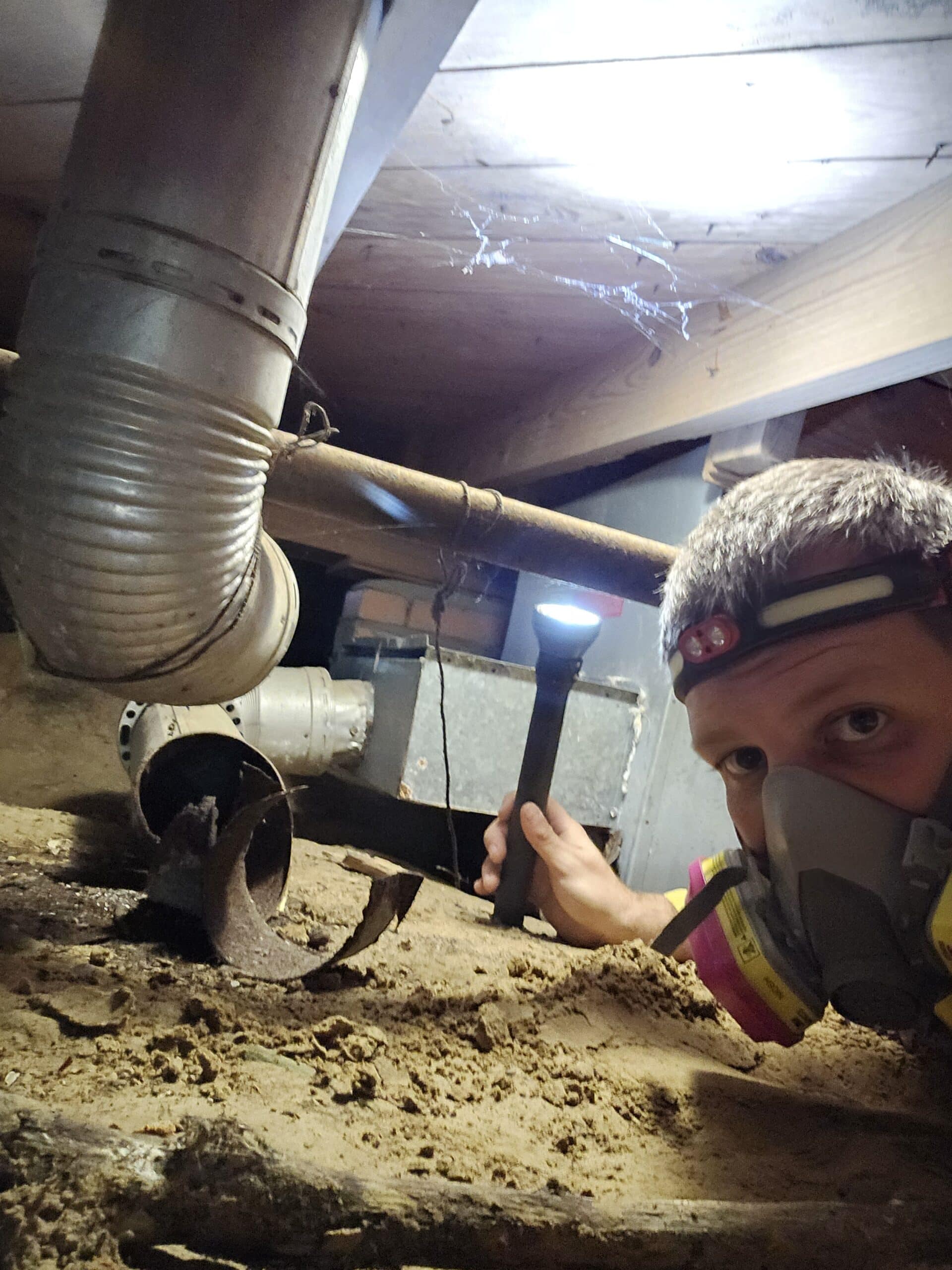 Inspector wearing respirator and headlamp examining a crawl space for termite or WDI activity in East Texas.
