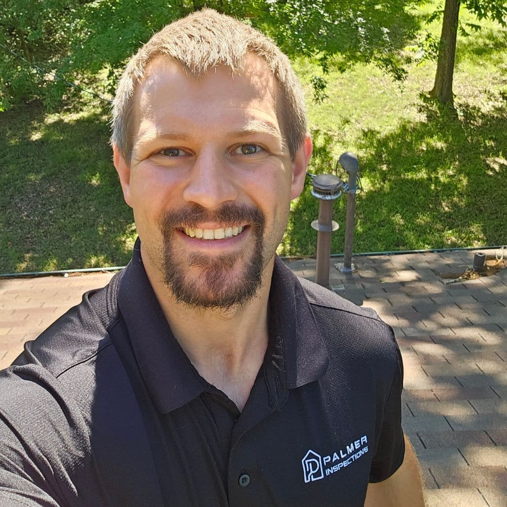 roof-home-inspection-expert-gilmer-tx A smiling Palmer Inspections professional standing on a residential shingle roof for a home inspection in Gilmer, TX.